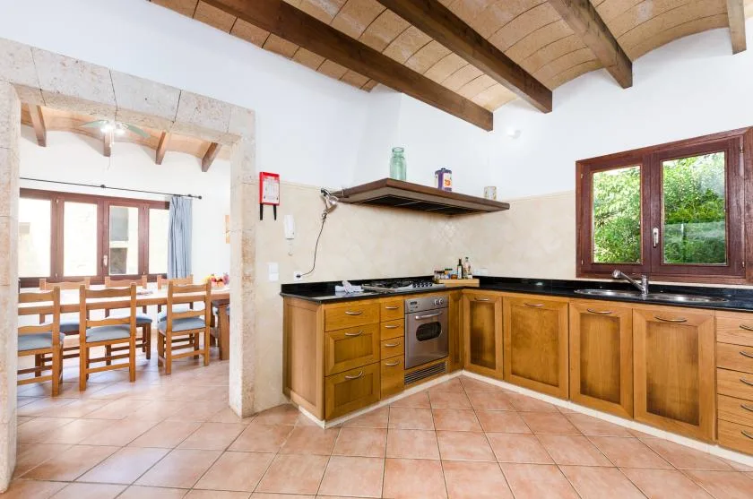 Una cocina con armarios de madera y un comedor visible a través de la puerta.