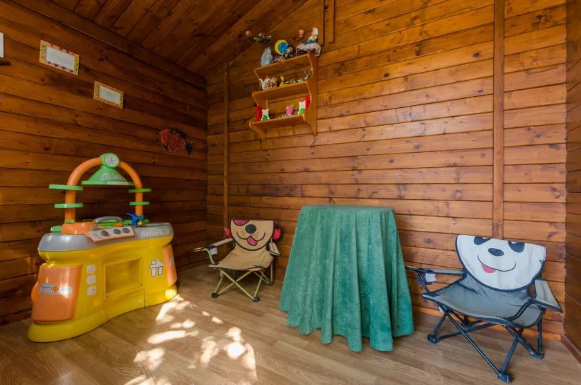 Un cuarto de juegos revestido de madera, con una cocina de juguete, asientos pequeños y una mesa cubierta.