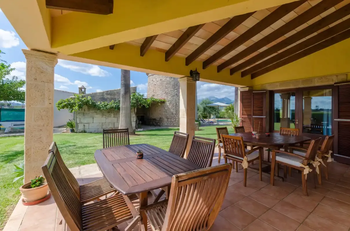 Una zona cubierta de comedor al aire libre con mesas y sillas de madera junto a un jardín.