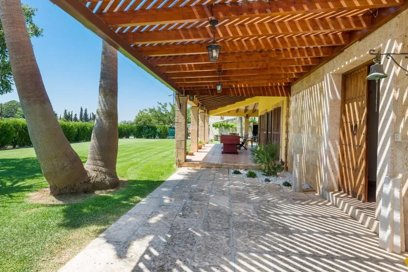 Un pasillo exterior sombreado junto al césped queda bajo una pérgola de madera.