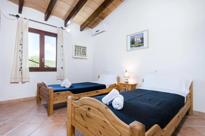 Un dormitorio con dos camas de madera, ropa de cama oscura y una ventana con cortinas.