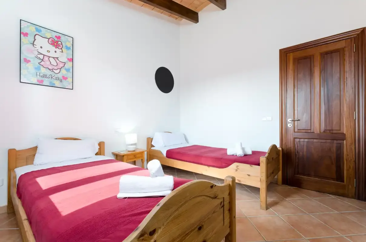 Un dormitorio con dos camas individuales, paredes blancas y una puerta de madera.