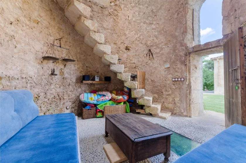 Interior rústico de piedra con asientos azules, una mesa de madera y una puerta abierta.