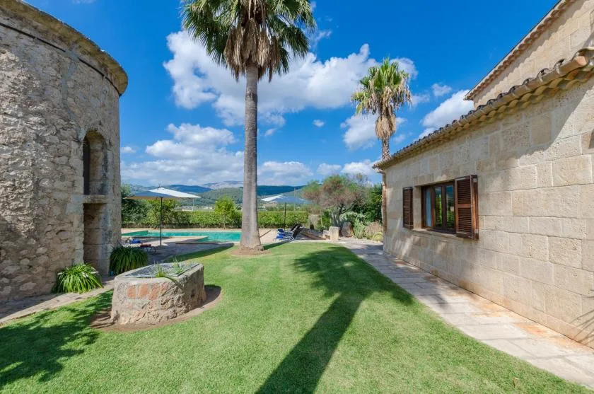 Un patio de césped se extiende entre edificios de piedra, con palmeras y una piscina.