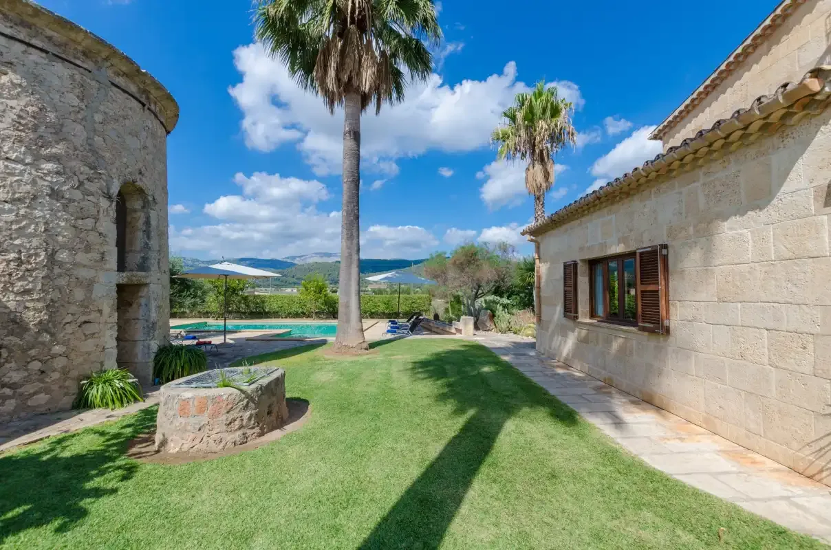 Un patio cubierto de césped entre edificios de piedra, con palmeras y una piscina.