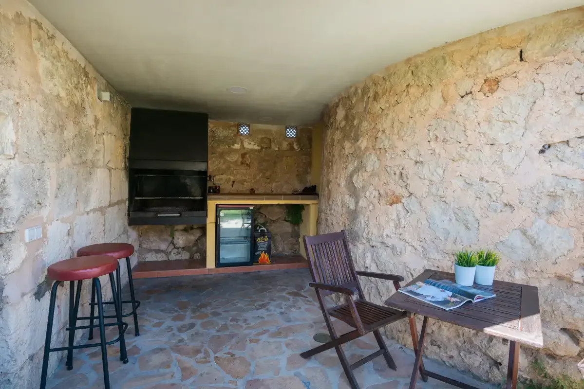 Un patio de paredes de piedra con una pequeña cocina y asientos al aire libre.