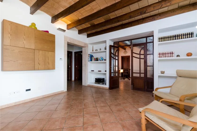 Una sala con suelo de baldosas, vigas de madera vistas y estanterías empotradas.