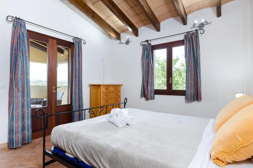 Un dormitorio con una cama doble, vigas de madera en el techo y ventanas con cortinas.