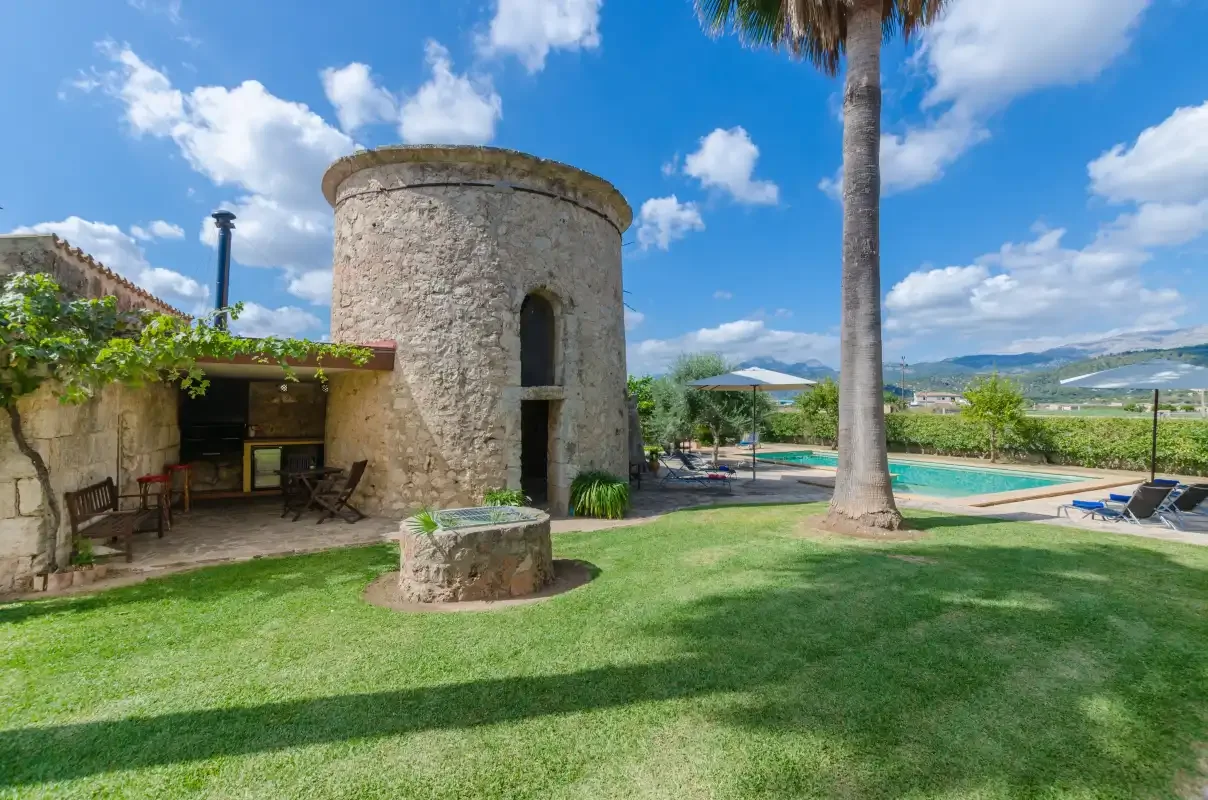 Una zona de piscina ajardinada con una torre de piedra y asientos a la sombra.