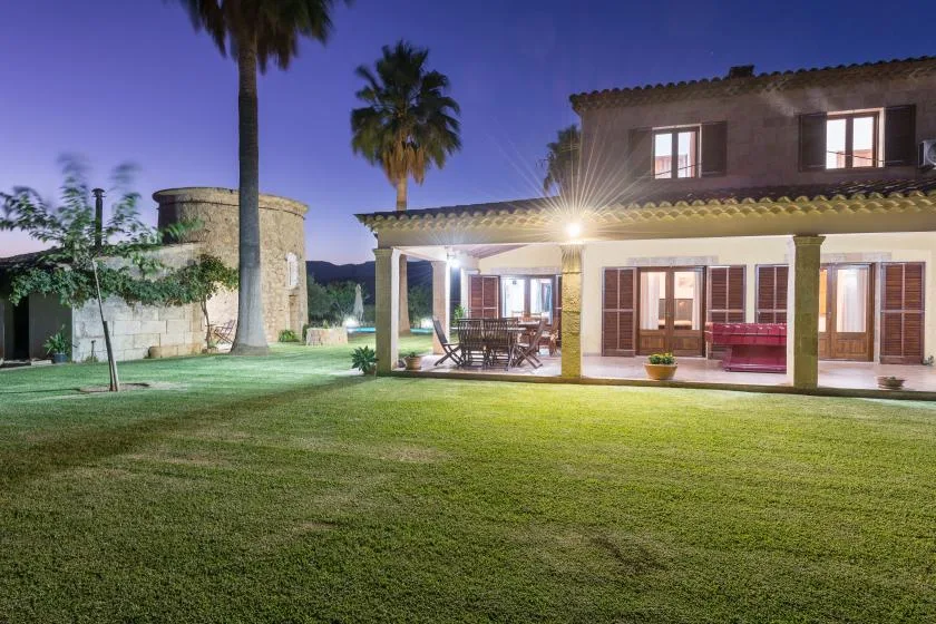 Una casa con patio cubierto da a un amplio césped bajo palmeras.