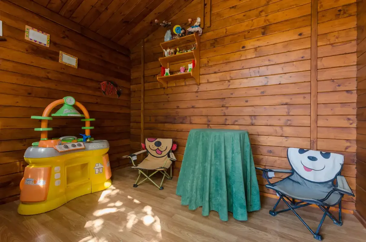 Una sala de juegos de madera con una cocinita, sillas pequeñas y una mesa cubierta.