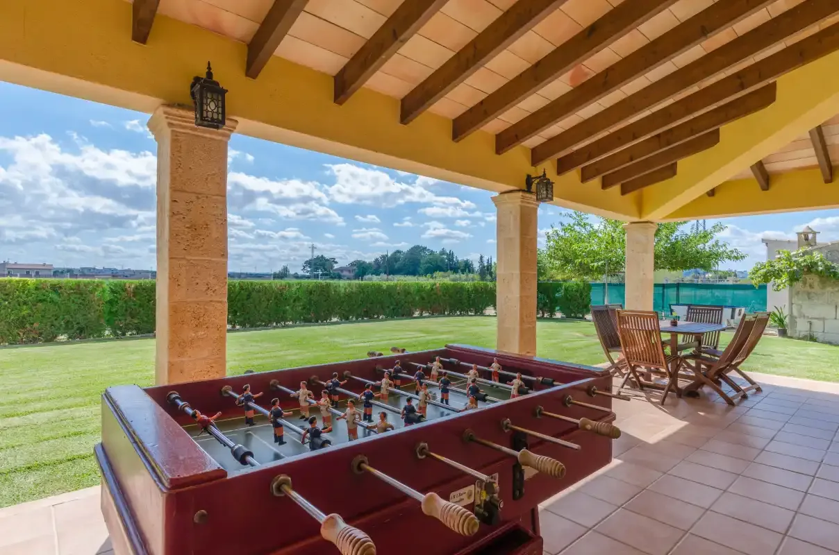 Un patio cubierto con un futbolín y asientos al aire libre da a un césped verde.