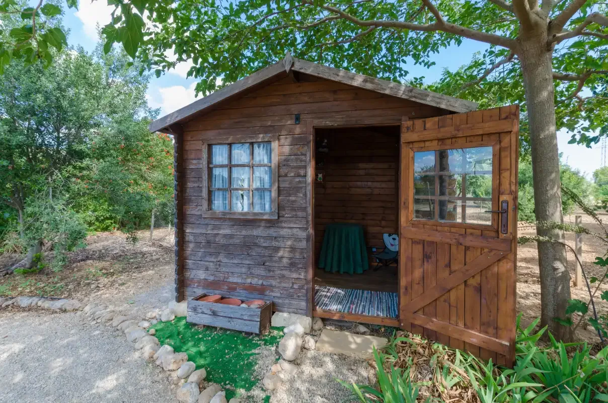 Una pequeña caseta de madera está entre árboles junto a un camino de grava.
