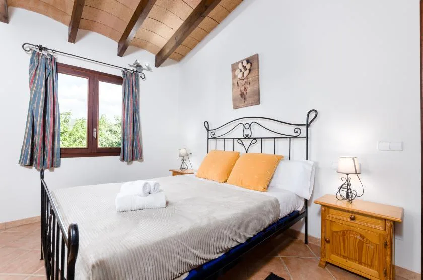 Un dormitorio con una cama de metal, almohadas naranjas y una ventana con cortinas.