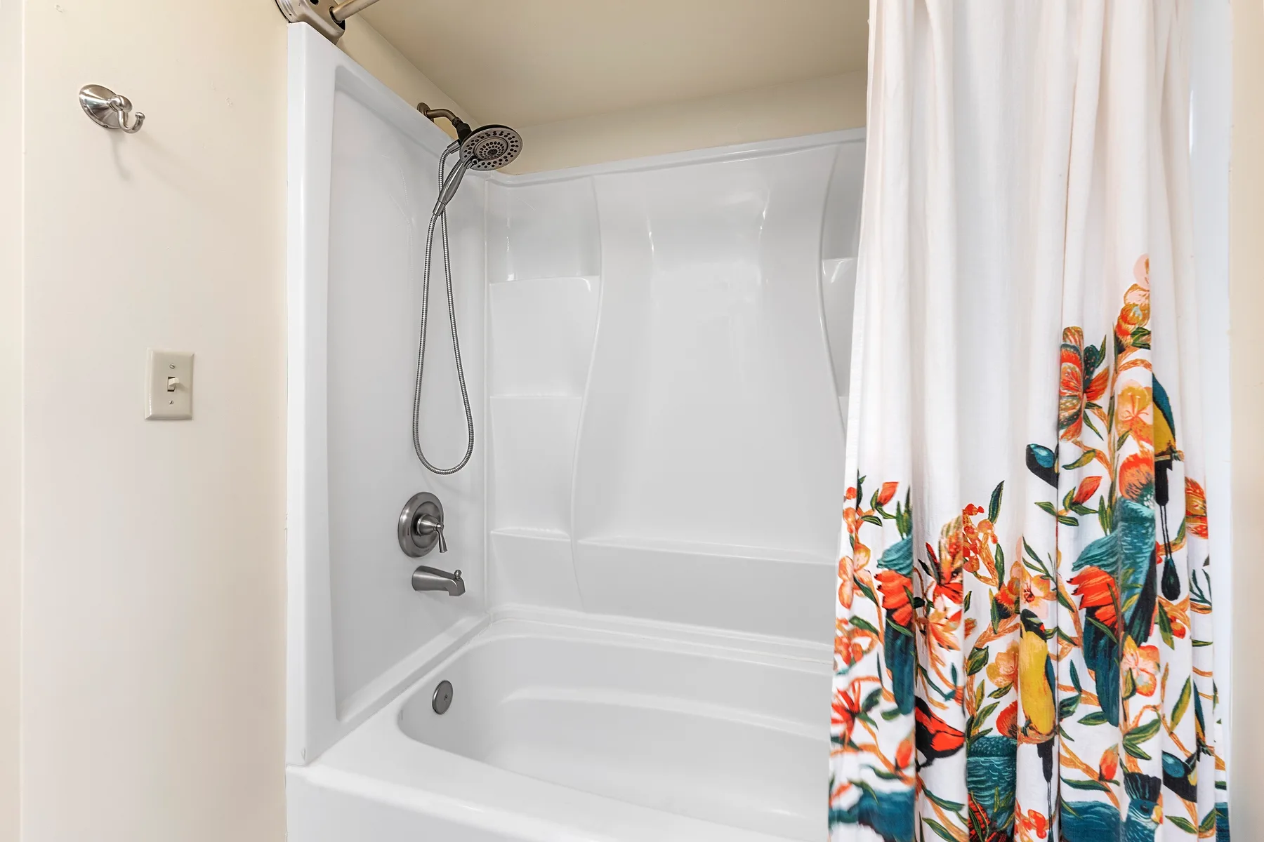 A bathroom shower and tub are partly covered by a colorful floral curtain.