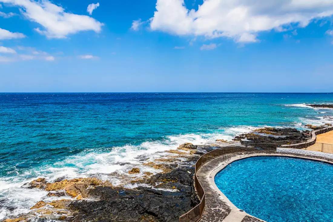 A swimming pool beside a rocky coastline, with waves breaking along the shore.