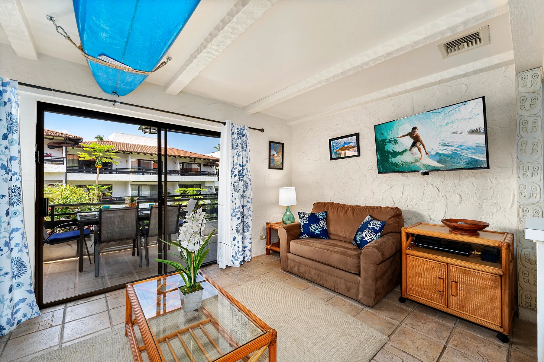 A living room with a brown sofa, glass coffee table, and sliding glass doors.
