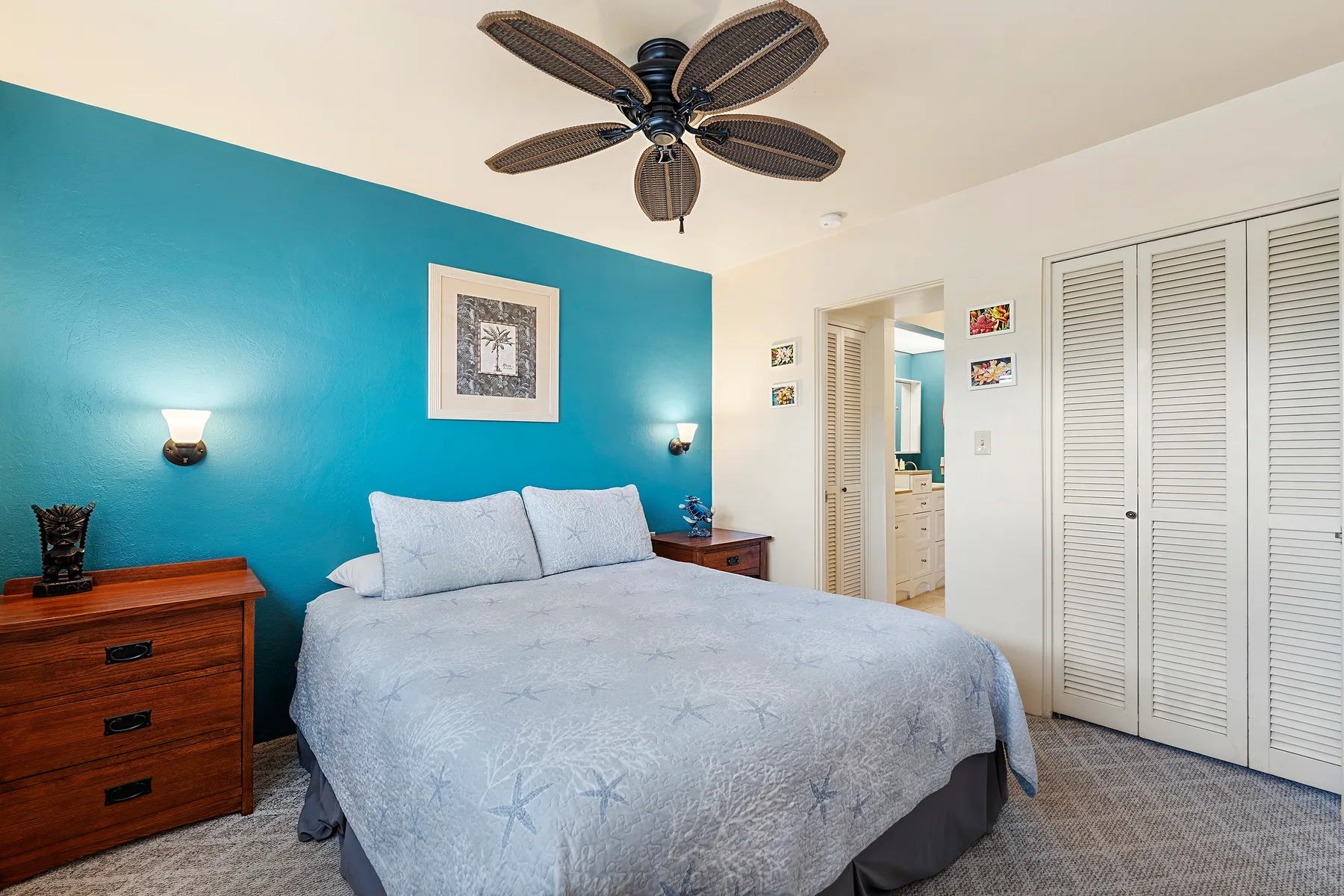 A bedroom with a bed against a teal wall and white louvered closet doors.