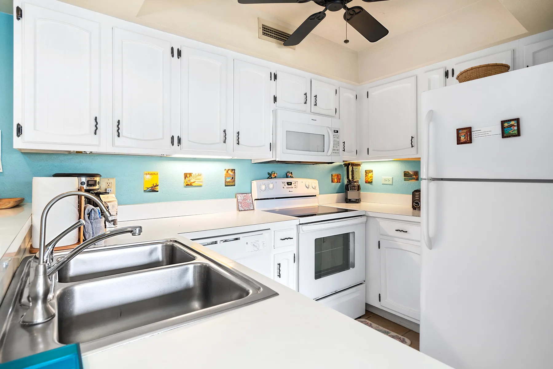 A bright kitchen with white cabinets, a stove, and a stainless steel sink.