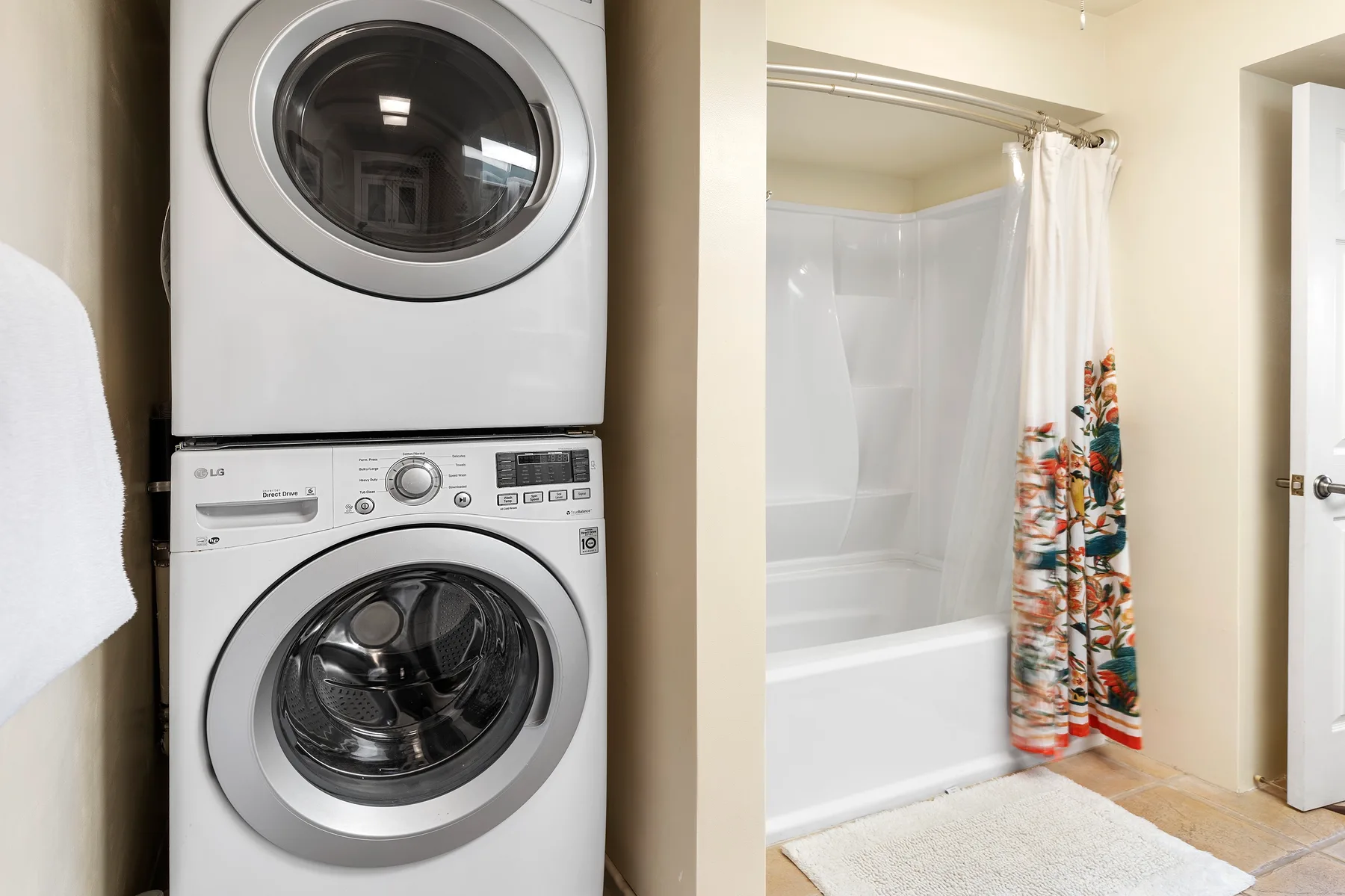 A laundry area with a stacked washer and dryer beside a bathtub with a colorful shower curtain.