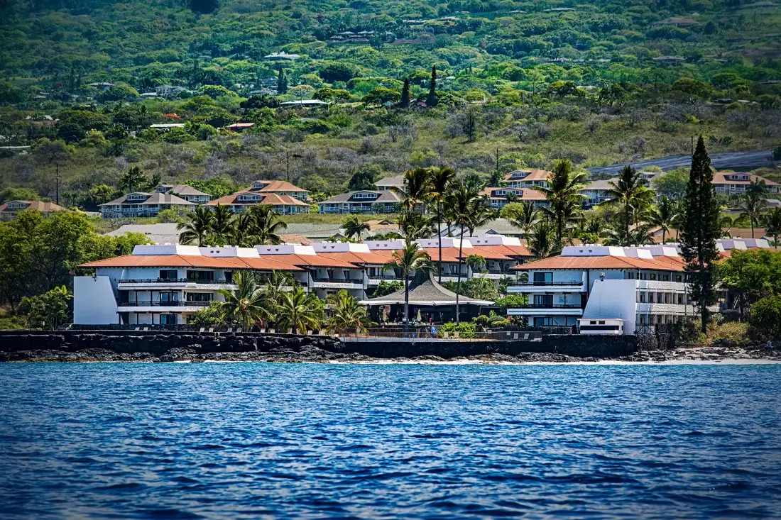 A coastal resort complex with palm trees stands beside the ocean.