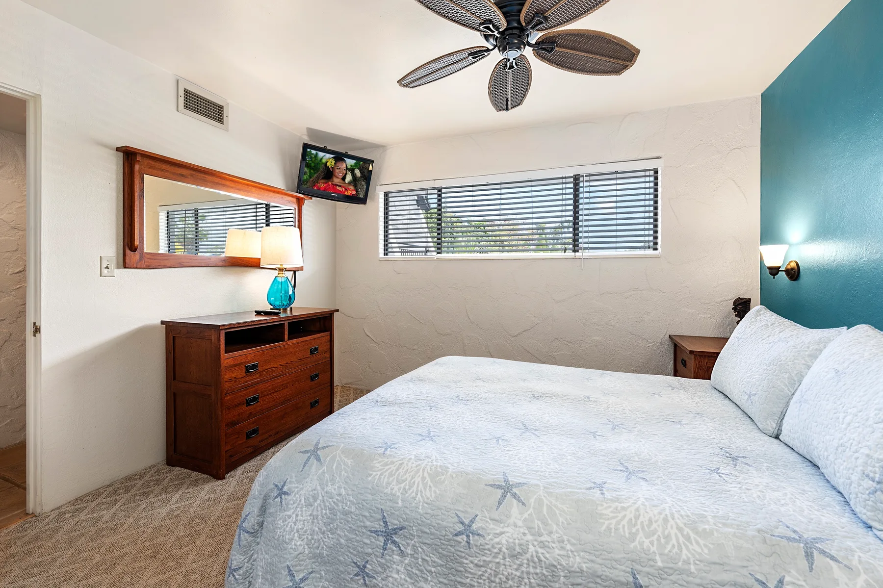 A bedroom with a bed, a wooden dresser, and a window with blinds.