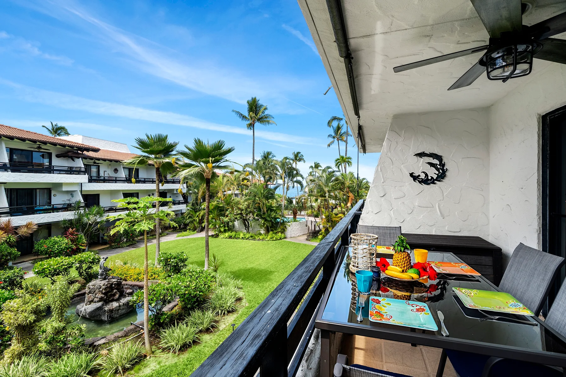 A balcony dining area overlooks a landscaped courtyard with palm trees.