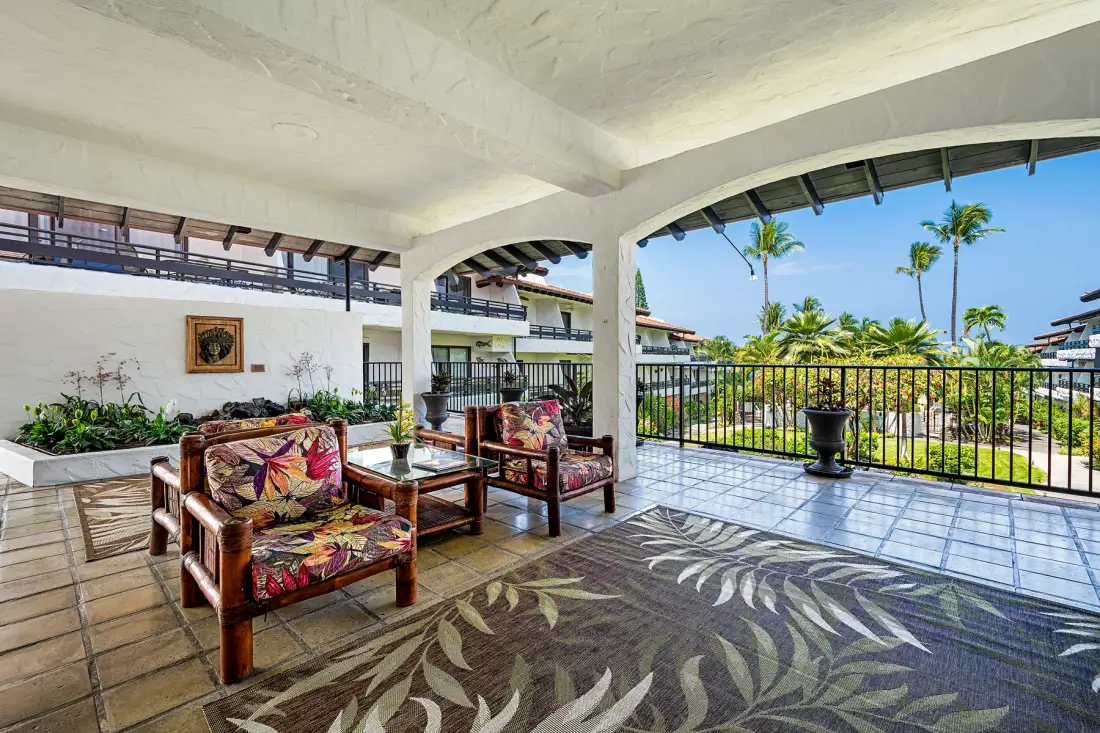 A covered outdoor seating area overlooks palm trees and greenery.