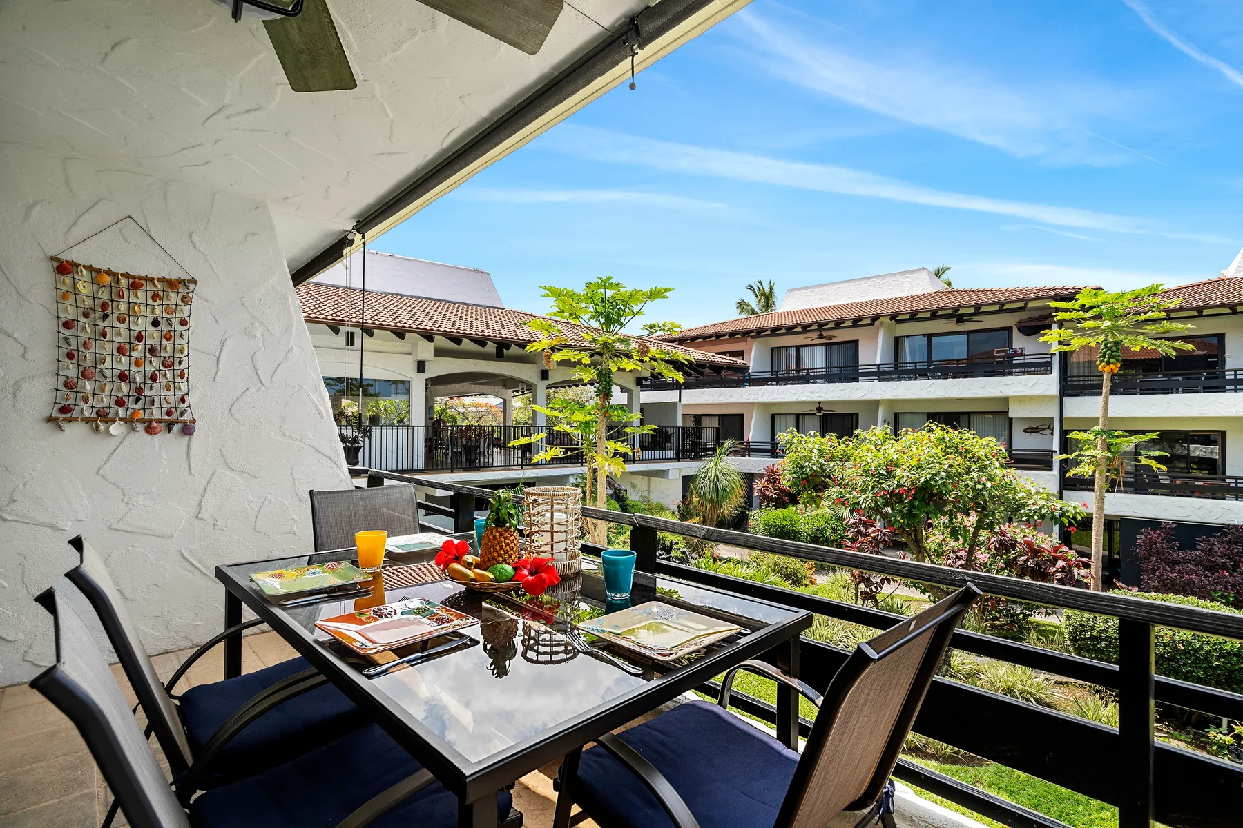 A covered outdoor dining area overlooks landscaped gardens and neighboring buildings.