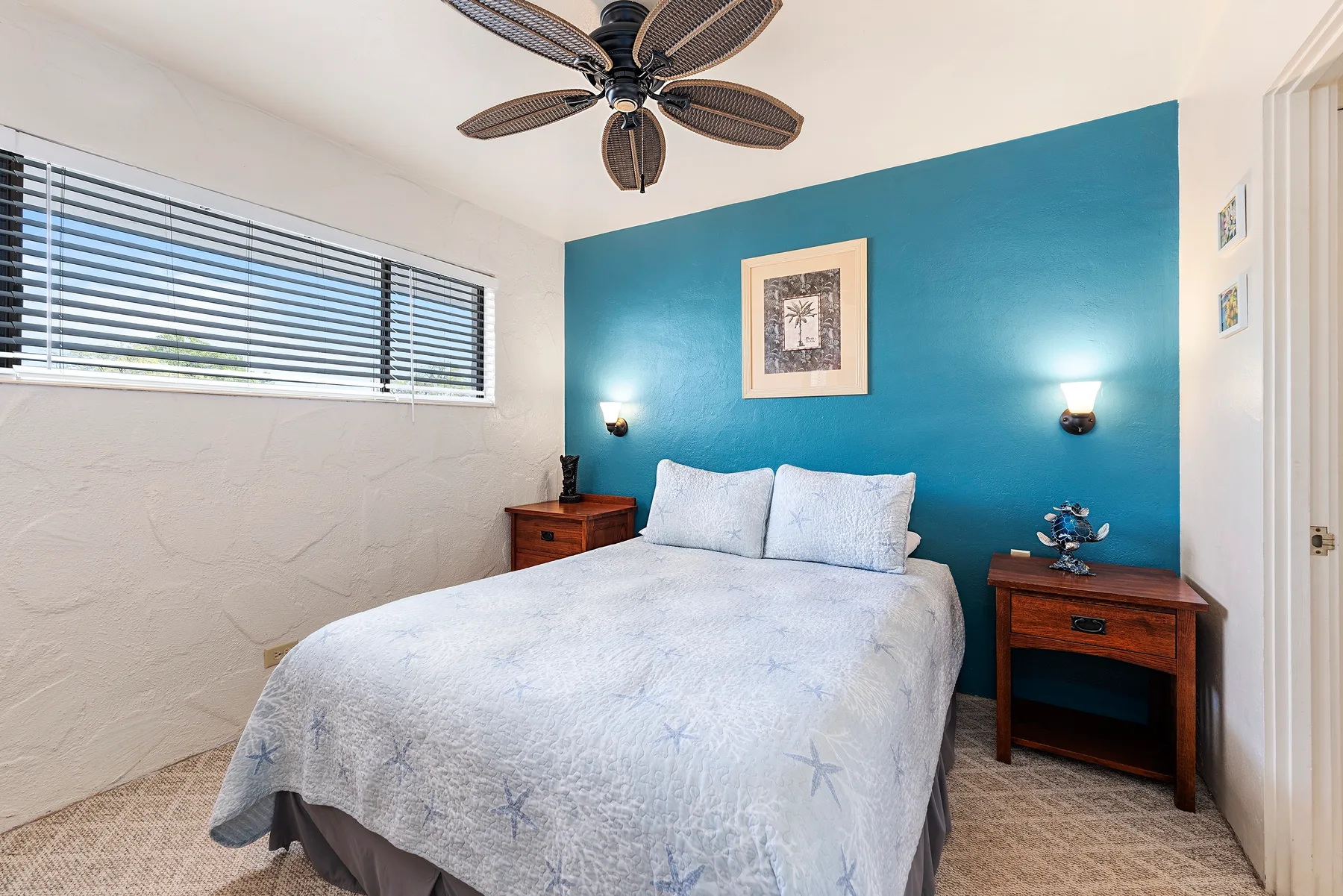 A bedroom with a bed against a blue accent wall and a window.