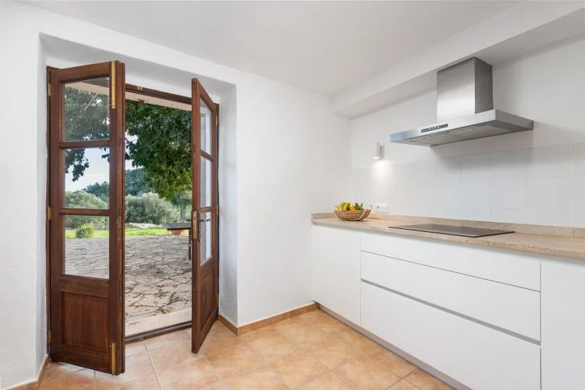 Una cocina luminosa con gabinetes blancos y una puerta abierta hacia un patio.