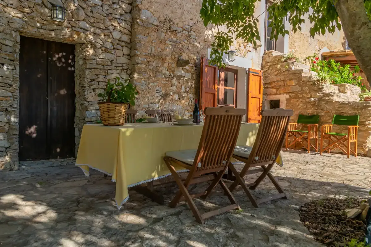 Un patio de piedra con una mesa de comedor al aire libre y asientos de madera.