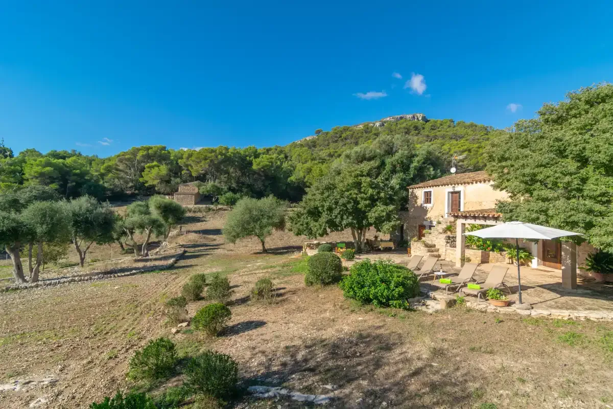 Una casa rural se encuentra junto a un jardín seco y colinas arboladas.