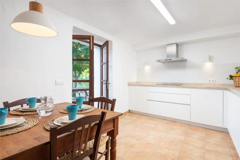 Una cocina luminosa con zona de comedor, mesa de madera y armarios blancos.