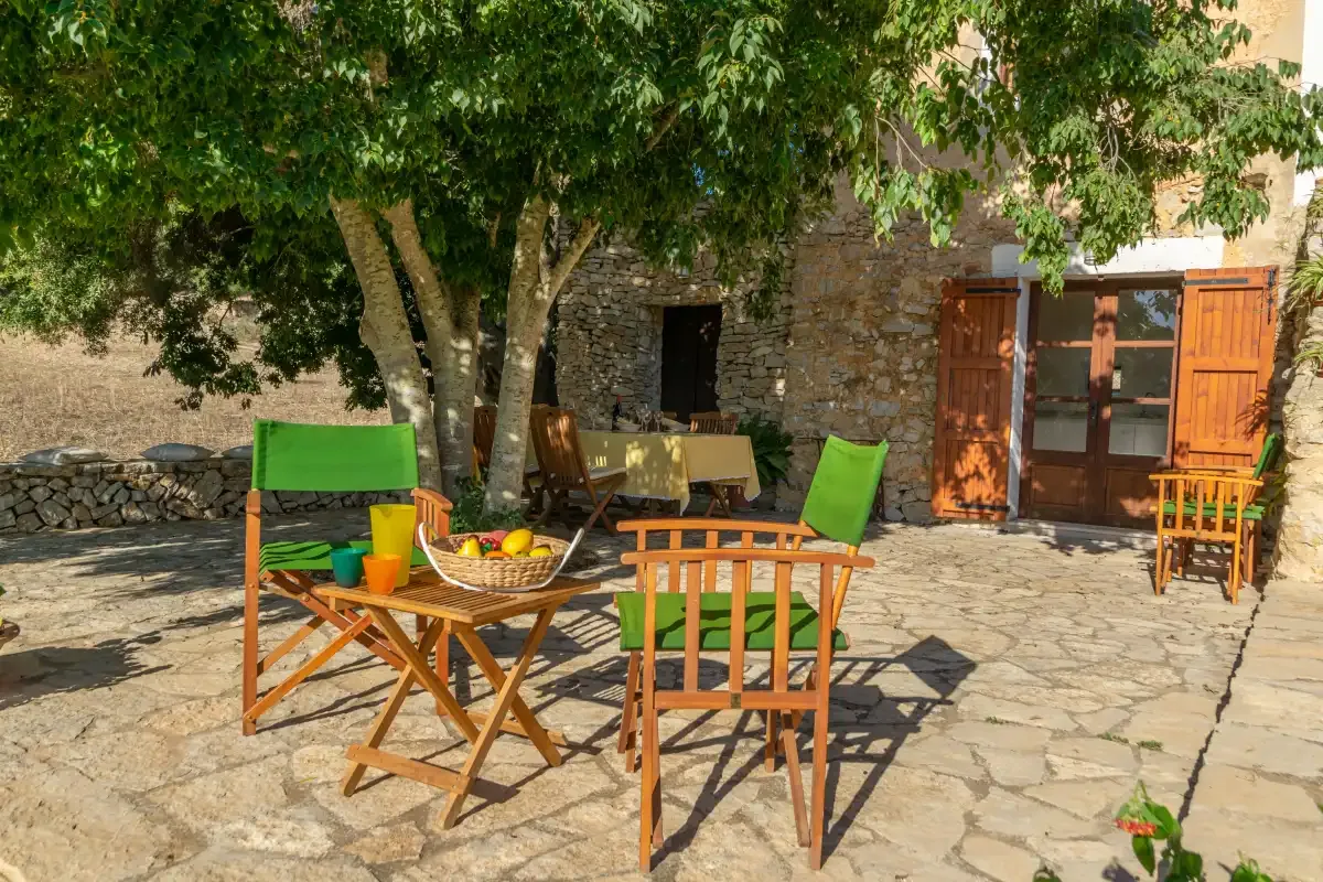 Un patio de piedra con asientos de cojines verdes y una mesa de comedor a la sombra.