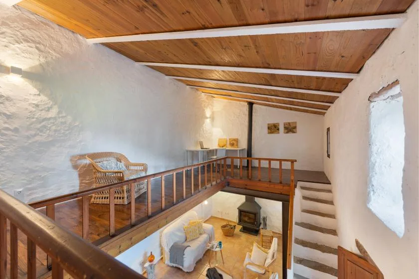 Una sala tipo loft con balcón de madera y escaleras bajo un techo de vigas de madera.