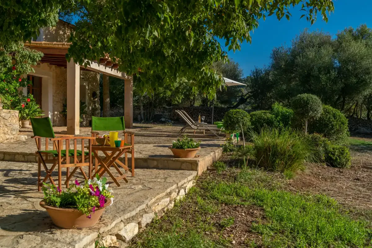 Una terraza de piedra con asientos al aire libre y flores en macetas junto a un jardín.