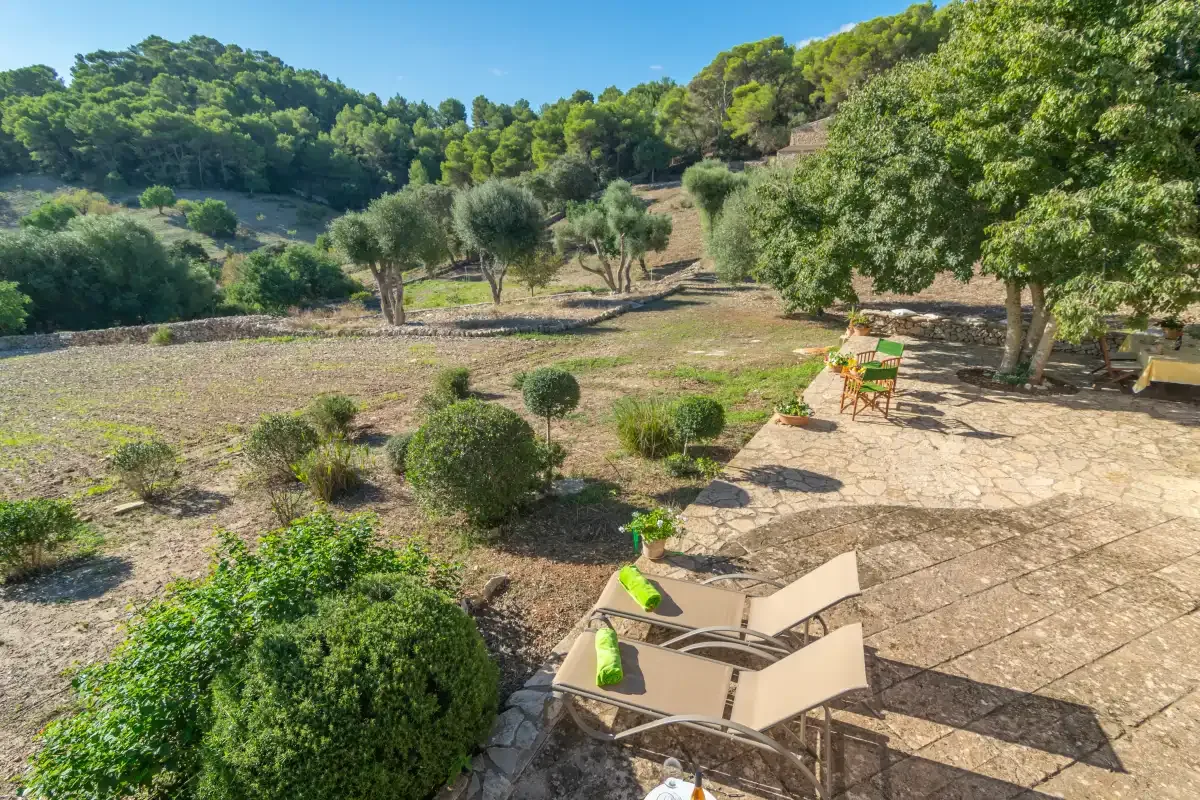 Un patio al aire libre con asientos de descanso da a un jardín y colinas arboladas.