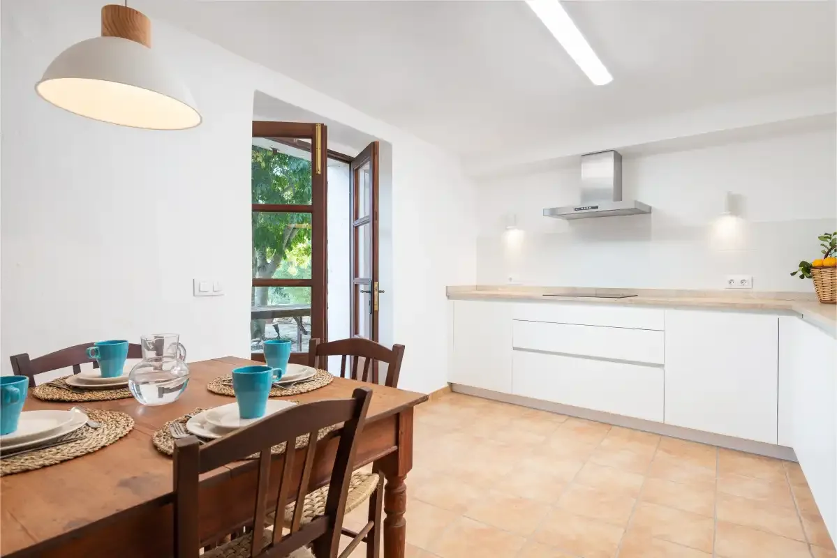 Una cocina luminosa con zona de comedor, mesa de madera y armarios blancos.