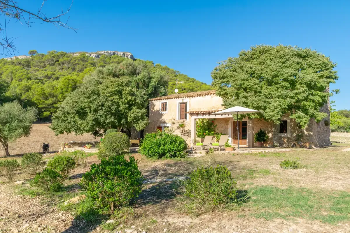 Una casa de piedra está rodeada de árboles en una ladera seca y despejada.