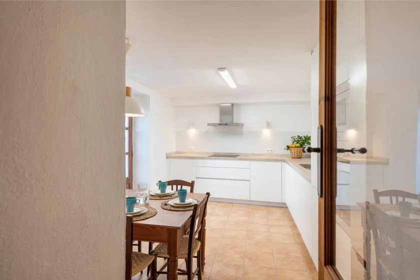 Una cocina luminosa con armarios blancos y una mesa de comedor en primer plano.