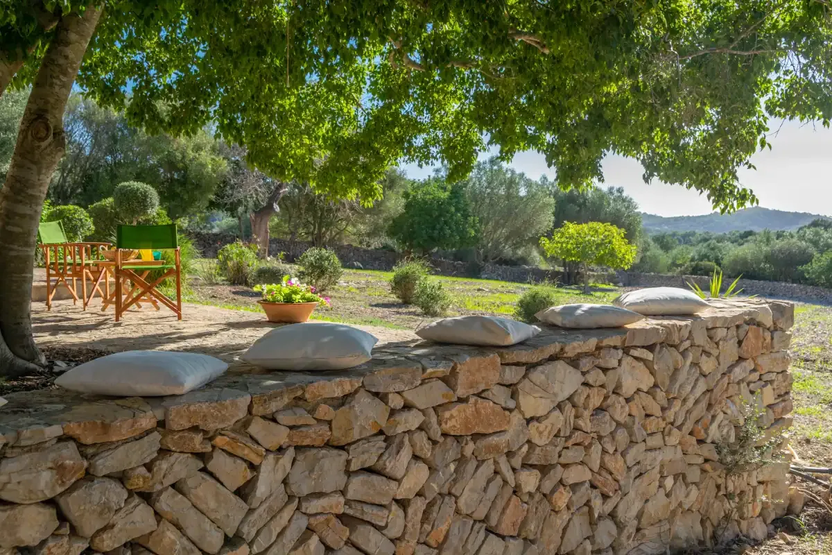 Una zona de descanso a la sombra con cojines sobre un muro bajo de piedra.