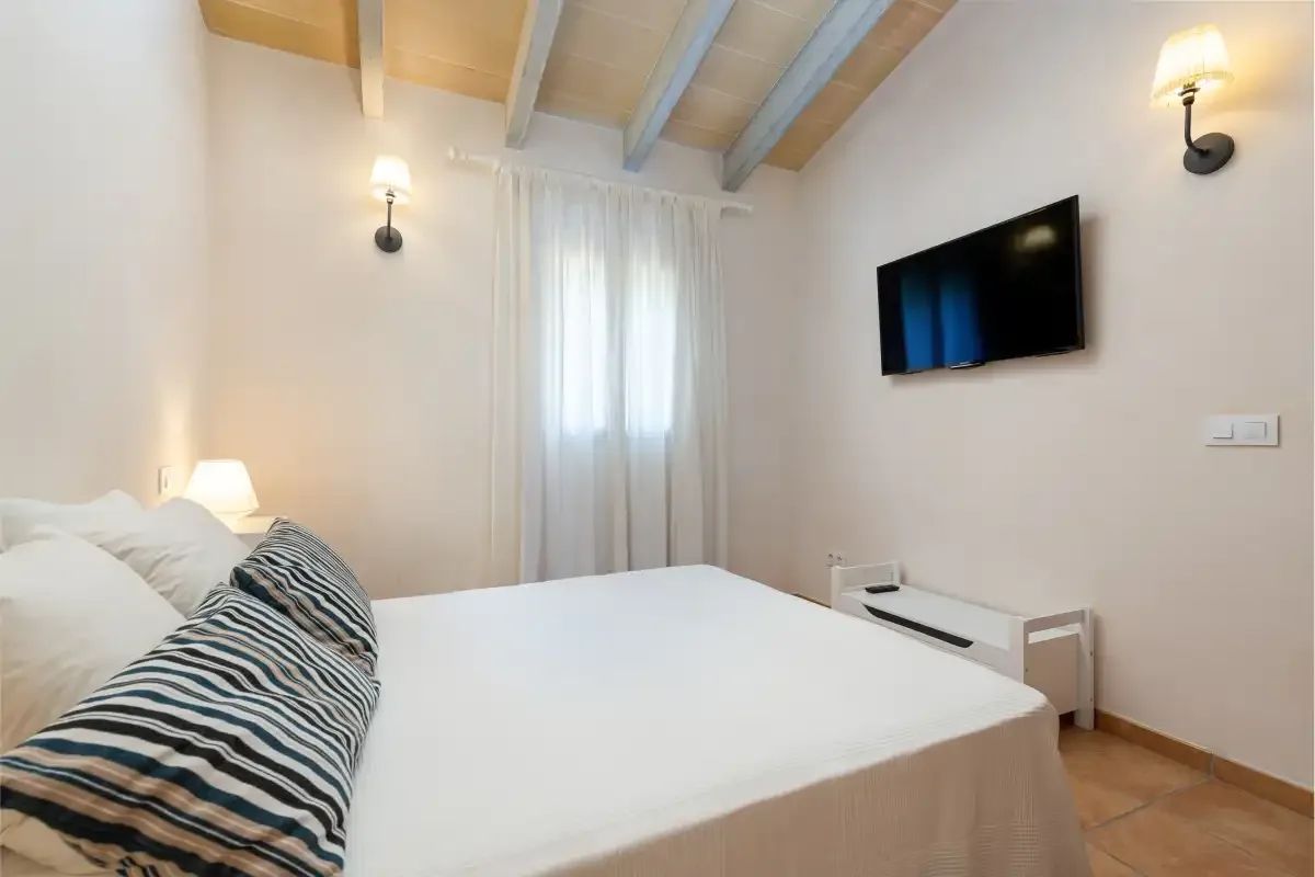 Un dormitorio con una cama, una ventana con cortinas y un televisor en la pared.
