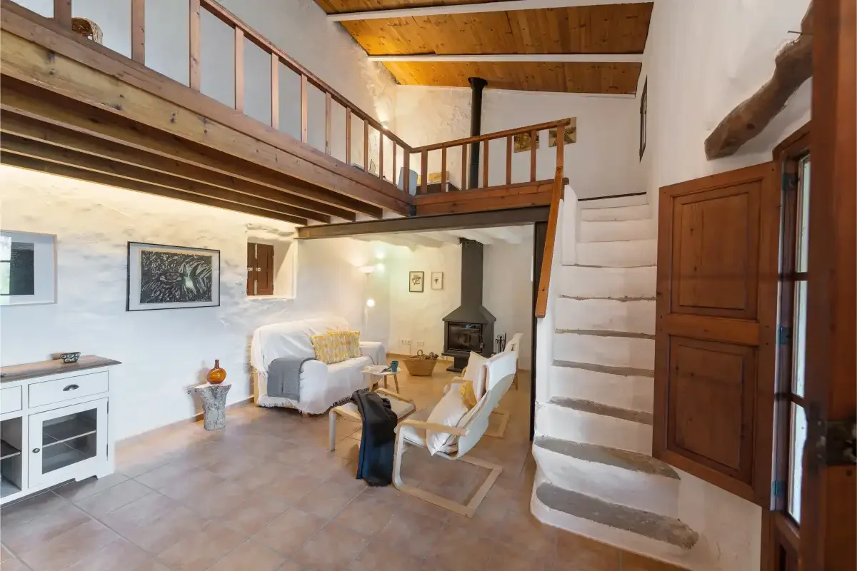 Una sala de estar rústica con asientos bajo un altillo de madera y junto a una escalera.