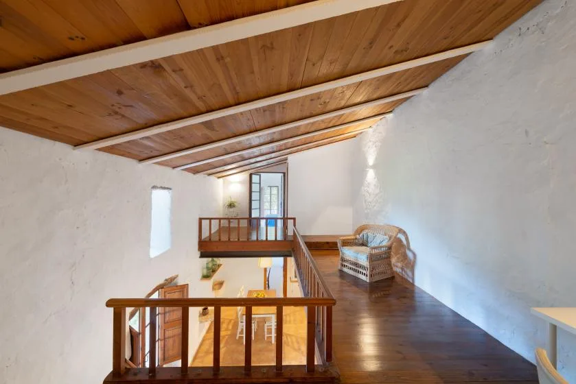 Un descansillo interior tipo loft con barandilla de madera, techo inclinado y zona de estar.