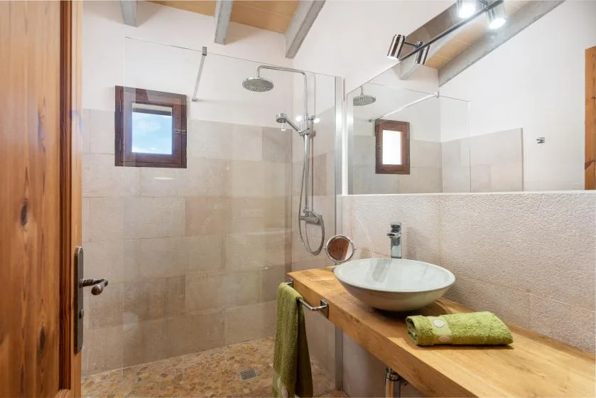 Un baño alicatado tiene una ducha de vidrio y un mueble de madera con lavabo sobre encimera.