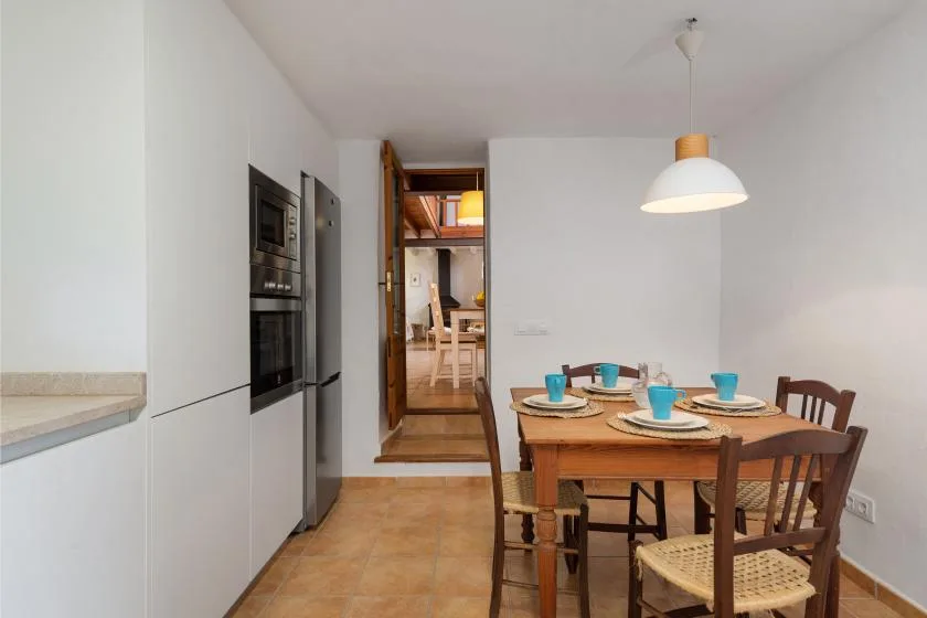 Comedor con una mesa de madera y sillas junto a una puerta que da a la cocina.