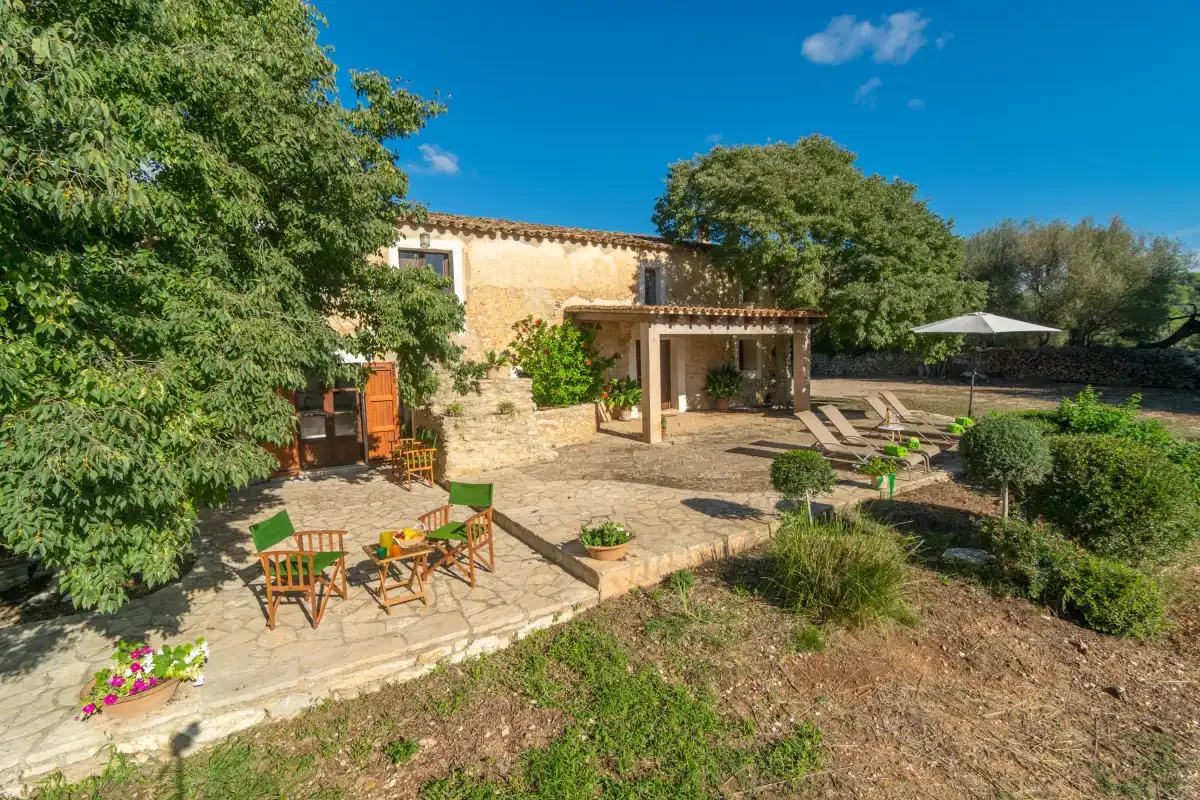 Una casa de piedra da a un patio soleado con asientos al aire libre y una terraza sombreada.