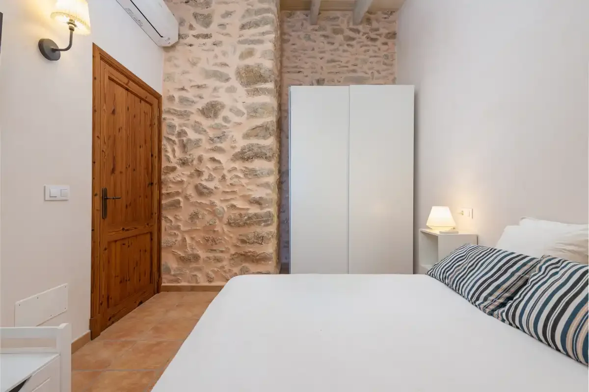 Un dormitorio con una cama blanca y una pared de piedra.