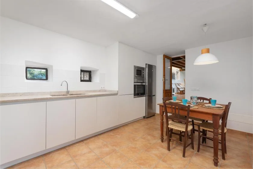 Una cocina y comedor luminosos con una encimera larga y una mesa de madera.